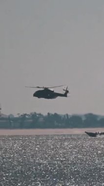 Askeri helikopter bir sürat teknesi ve bir savaş gemisinin üzerinde alçaktan uçuyor.
