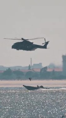 Askeri helikopter bir motorbotun yanında denizin üzerinde uçuyor.