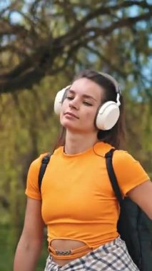 Sıradan bir genç kadın, yeşil bir parkta rahatlama yürüyüşü sırasında kulaklıkla müzik dinlemekten hoşlanır.