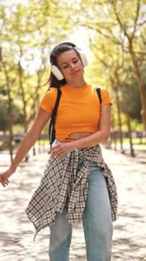 Parkta müzik dinleyen ve dans eden tasasız bir öğrenci.