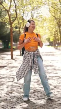 Kulaklıkla müzik dinleyen ve parkta dans eden mutlu bir öğrenci.