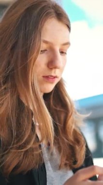 Sarışın kadın tren istasyonunda beklerken akıllı telefon kullanıyor.