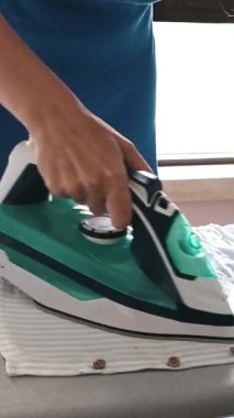 Ev hanımı ütü masasında beyaz çizgili bir gömlek ütülüyor.