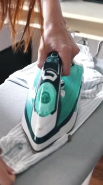 Ev hanımı ütü masasında çizgili gömlek ütülüyor.