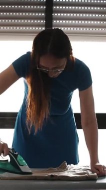 Ev hanımı ütü masasındaki kıyafetleri ütülüyor.