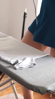Ev hanımı ütü masasındaki beyaz tişörtü ütülüyor.