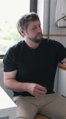 Siyah tişört giyen ve haki pantolonlu bir adam mutfak lavabosunda patates yıkıyor.