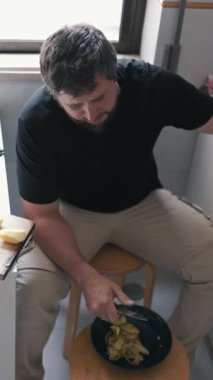 Adam kasede patates soyuyor, modern bir mutfakta taburede oturuyor.