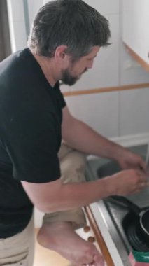 Adam bulaşıkları titizlikle parlak bir mutfakta yıkıyor ve ev temizliğini gösteriyor.