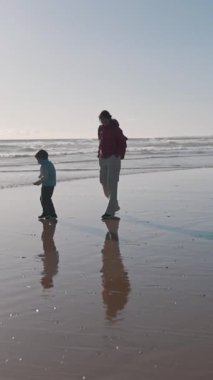 Anne ve oğlu gün batımında kumsalın ıslak kumlarında huzurlu bir yürüyüşün tadını çıkarıyorlar.