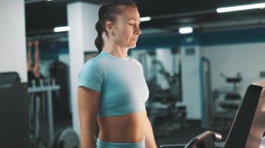 Kararlı atletik kadın kardiyo antrenmanı yapıyor, spor salonunda koşu bandında yürüyor.