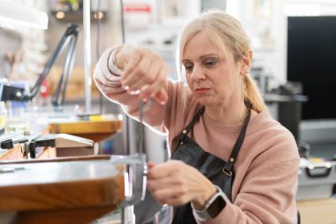 Parlak bir atölyede metal bileşenlerini dikkatlice ölçen odaklanmış usta kadın.