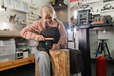 Kadın sanatkar konsantre oluyor, stüdyosunda çekiç ve yumrukla metal şekillendiriyor.