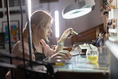 Zanaatkar ayrıntılı işlere odaklanıyor, küçük bir meşale kullanarak el yapımı mücevherler yapıyor.