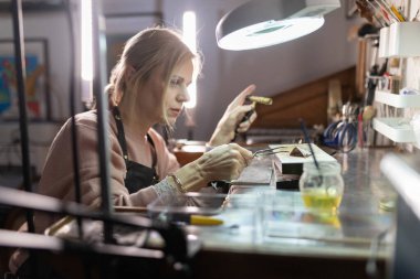 Kadın kuyumcu atölyesinde meşaleyle hassas bir metal parçayı lehimlemeye odaklanmış.