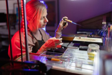 Kadın, atölyesinde özel mücevherler yaparken metal parçaları dikkatlice lehimliyor.