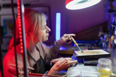 Kuyumcu, parlak odaklı ışık altında meşale kullanarak bir metal parçası üzerinde dikkatlice çalışıyor.