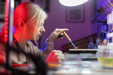 Kadın sanatkar konsantre oluyor, atölyesinde meşale ateşiyle metal bir parça şekillendiriyor.