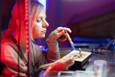 Kadın kuyumcu dinamik atölye ortamında titizlikle metal lehimliyor.