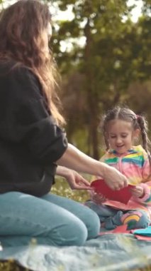 Anne ve kızı güneşli bir parkta renkli kağıt kalplerle oynayarak birlikte kaliteli vakit geçirmekten zevk alıyorlar.