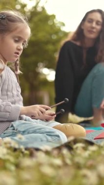 Genç kız annesiyle çayırda davul çalmayı öğreniyor.