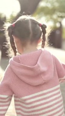 Parkta yürürken ebeveynin elini tutan genç kız.