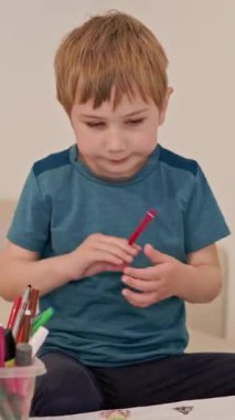 Evde renkli kalemlerle kağıda resim çizen konsantre çocuk.