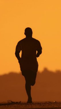 Gün batımında sahilde koşan bir adamın silüeti.