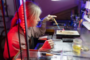 Kadın kuyumcu, yaratıcı bir atölyede metal lehimlemek için meşale kullanıyor.