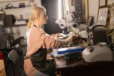 Kadın kuyumcu titizlikle mikroskop kullanarak bir mücevher üzerinde çalışıyor.