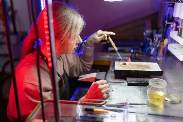 Kadın kuyumcu, yaratıcı bir atölyede metal lehimlemek için meşale kullanıyor.