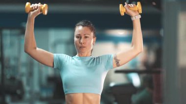 Atletik kadın modern bir spor salonunda dambıl gibi omuz egzersizi yapıyor.