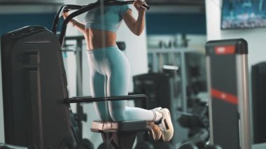 Kararlı kadın sırt kası gelişimi için bir makine üzerinde destekli barfiks egzersizi yapıyor.