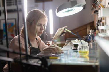 Tezgahındaki metal bir nesne üzerinde kaynak makinesiyle çalışan kadın bir zanaatkar.