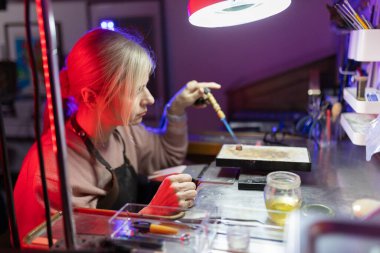 Esnaf kadın, metali mikro meşaleyle ısıtıyor ve özel el yapımı mücevherler yapıyor.