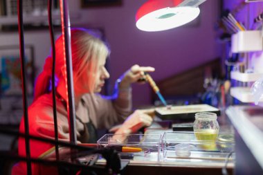 Detaylara odaklanan zanaatkar bir kadın atölyede el yapımı mücevher yapmak için kaynak makinesi kullanıyor.