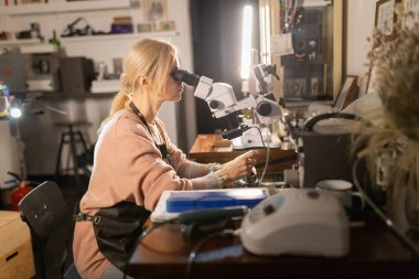 Atölyede mikroskopla incelik ve ustalık üzerine çalışan usta bir zanaatkar.