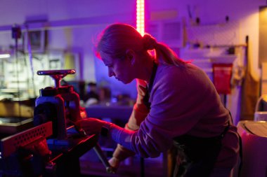 Kadın sanatına odaklanıyor, canlı, neon ışıklı bir atölyede ameliyat aletleri kullanıyor.