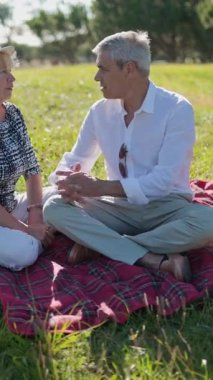 Yaşlı bir çift, sakin bir park ortamında piknik battaniyesinde eğleniyor.