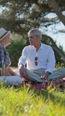 Yaşlı çift boş vakitlerin tadını çıkarıyor, doğanın ortasında piknik battaniyesinde sohbet ediyorlar.