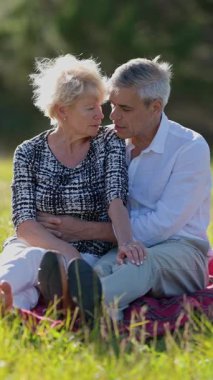 Yaşlı çift, çayır piknik battaniyesinde samimi anlar paylaşıyor.