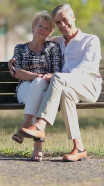 Sevecen yaşlı çift parkta huzurlu bir günün tadını çıkarıyor, bankta oturuyor ve samimi anlarını paylaşıyor.