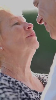 Yaşlı çift dışarıda romantik bir anın tadını çıkarıyor, burunları birbirine dokunuyor, sevgi ve bağlılık gösteriyor.
