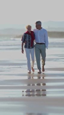 Yaşlı çift sahilde romantik bir yürüyüş yapıyor.