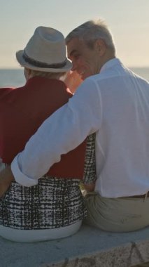 Sevecen yaşlı çift okyanusun kenarında huzurlu bir gün batımının tadını çıkarıyor.