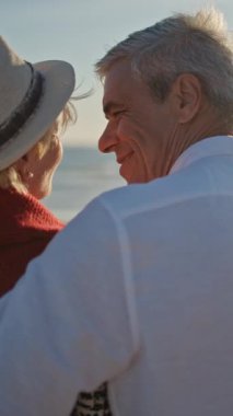 Yaşlı çift gün batımında deniz kenarında romantik bir anın tadını çıkarıyor.