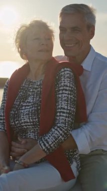 Yaşlı çift gün batımında sahilde romantik bir anın tadını çıkarıyor.