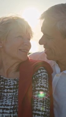 Yaşlı çift gün batımında sahilde romantik bir anın tadını çıkarıyor.