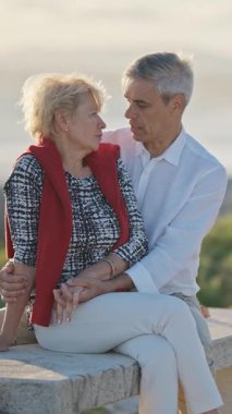 Yaşlı bir çift bankta romantik bir anın tadını çıkarıyor. Arka planda okyanus varken birbirlerinin gözlerine bakıyorlar.