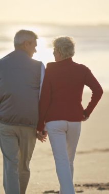 Emekli çift güzel bir gün batımında sahilde romantik bir yürüyüş yapıyor.